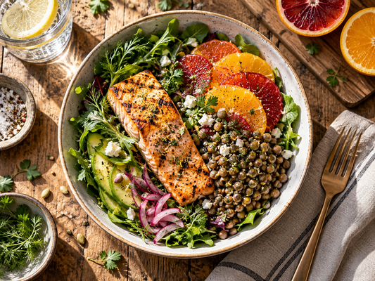 Grilled salmon salad bowl with lentils, leafy greens, avocado, and fresh citrus slices on a rustic wooden table.