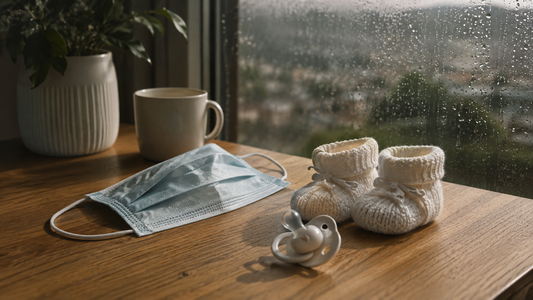 Blue face mask, white baby booties, and pacifier on a wooden table representing pandemic uncertainty and family planning